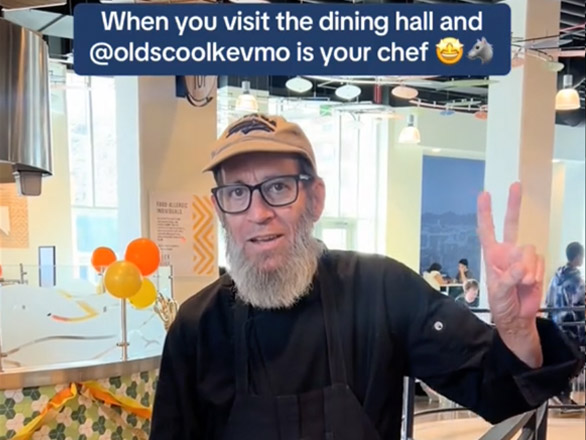 Screenshot from University of Nevada, Reno Tik Tok account showing KevMo wearing a Nevada Sport Wolf cap and giving a peace sign at a dining hall. The caption reads "When you visit the dining hall and @oldschoolkevmo is your chef."