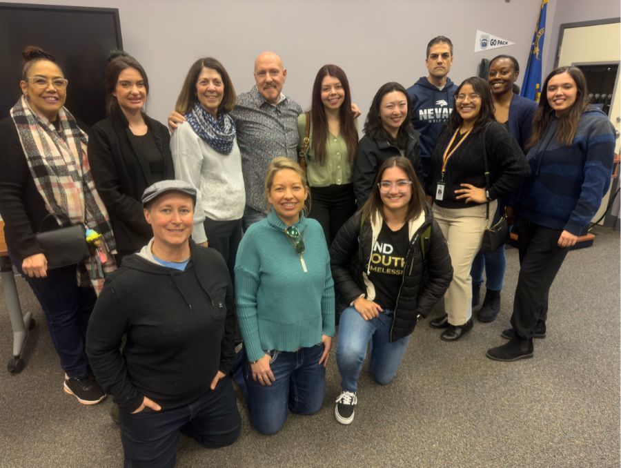 A group of thirteen colleagues smiling and posing together for a photo in a modern office setting.