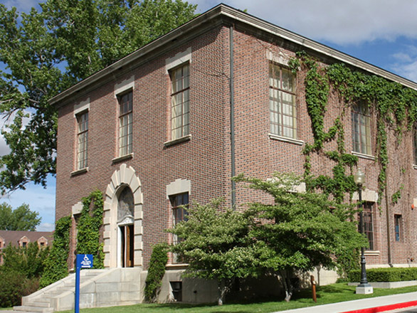 A view of Clark Administration building, a multistory brick building with multiple windows on each floor, a large entry way staircase, and vines hanging from the building.