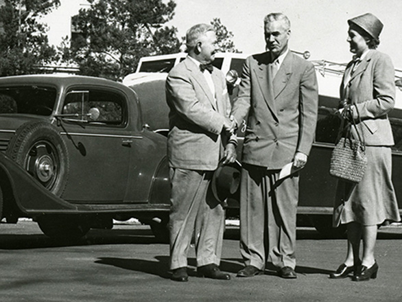 Black and white image of Arthur K. Bourne (left), University President Malcolm Love (center), and Mrs. Alberta Bourne (right) stand in front of the donated Buick Aerocar car and the Zephyr trailer