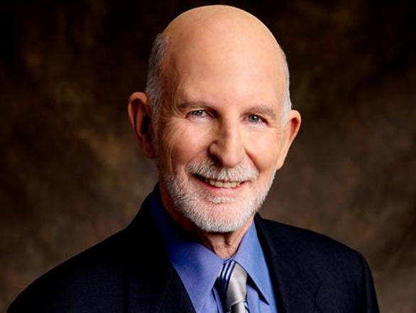 Milton Glick wearing a blue suit, shirt and tie smiling at the camera