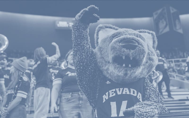 Nevada mascot in a number 14 jersey raising its fist in an arena crowd in a monochromatic blue treatment.