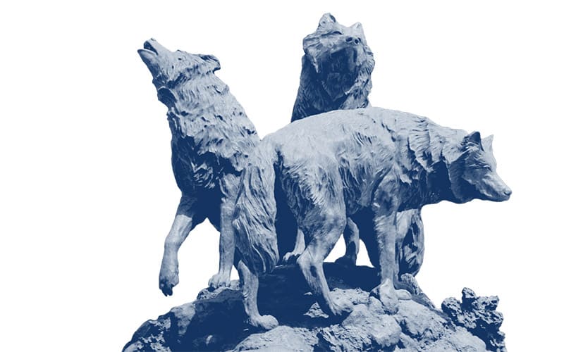 Monochromatic navy blue duotone cut-out of the bronze wolf pack statue showing three wolves gathered on boulders, one howling toward the sky.