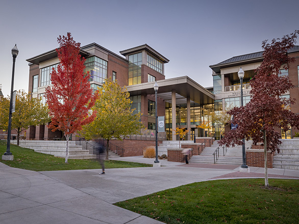 Exterior view of the Pennington Student Achievement Center at dusk framed by autumn trees with red and yellow foliage and tiered outdoor concrete steps.