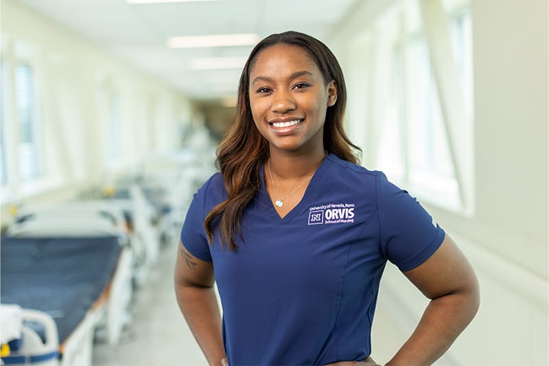 Nursing student smiling in clinical navy scrubs in a patient simulation lab