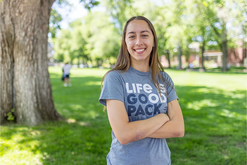 Undergraduate student standing on the historic Quad wearing a gray Life is Good Pack t-shirt