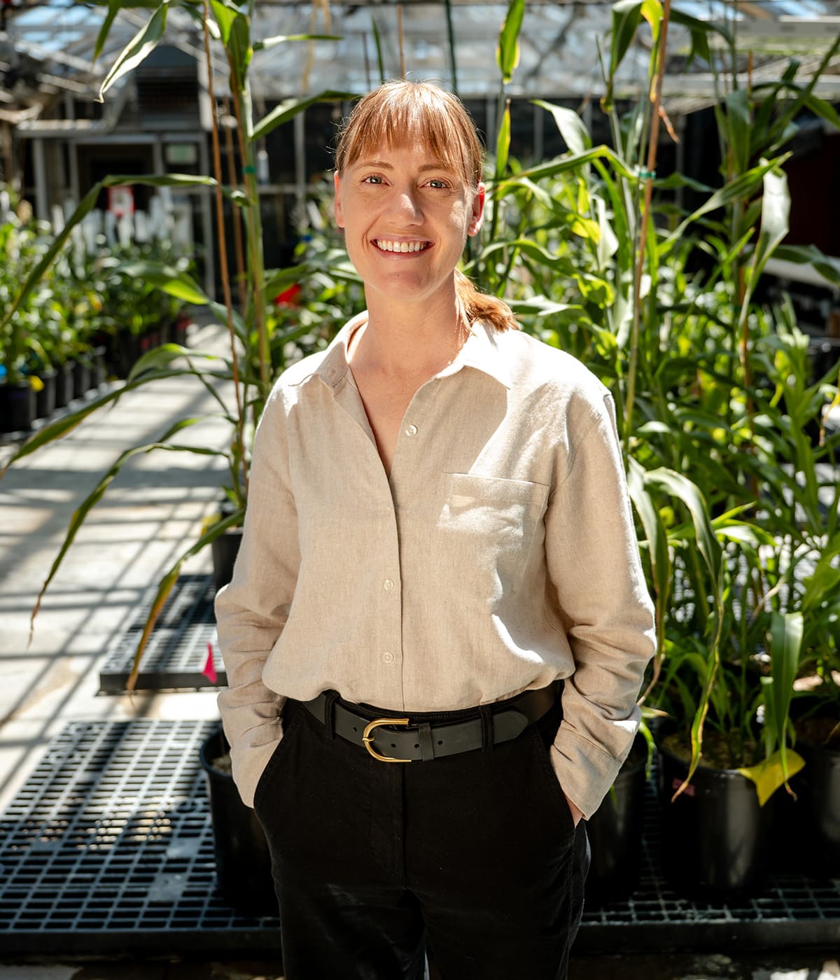 Agricultural researcher smiling in a sunlit campus greenhouse surrounded by research plants