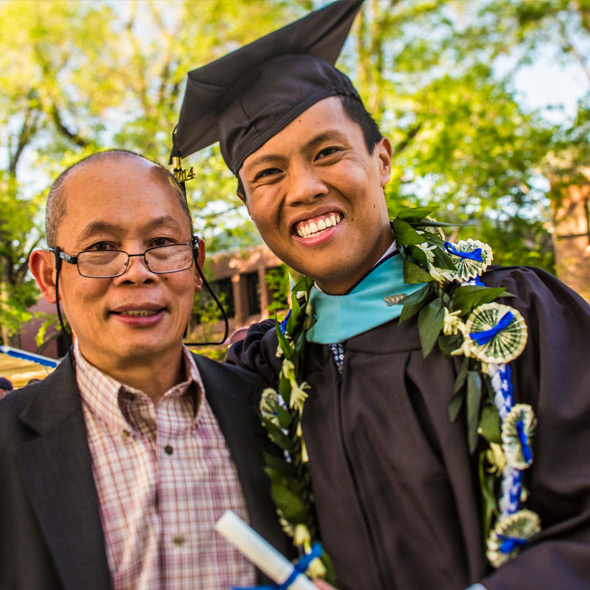 Graduating male student smiling with father during spring commencement