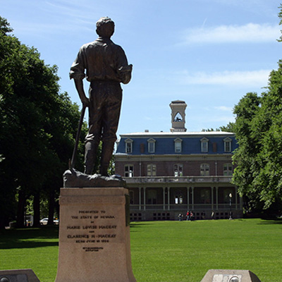 The statue of John Mackay is seen from behind with the University quad lined with trees in the distance and Morrill Hall in the background