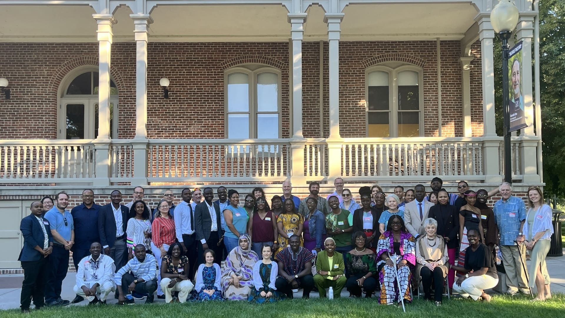 A group of 27 people gathered on the grass of north campus smiling for a group photo.