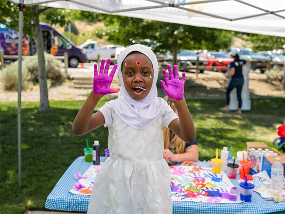 A young girl in a white dress with purple paint on her palms at World Refugee Day.