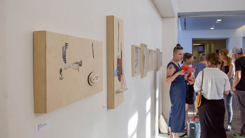 A gallery space with art hanging and people looking at the pieces.