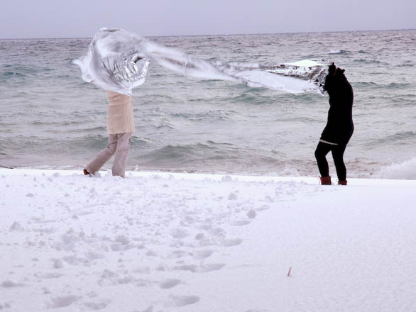 Two people hold a piece of fabric on the snowy shores of Lake Tahoe.