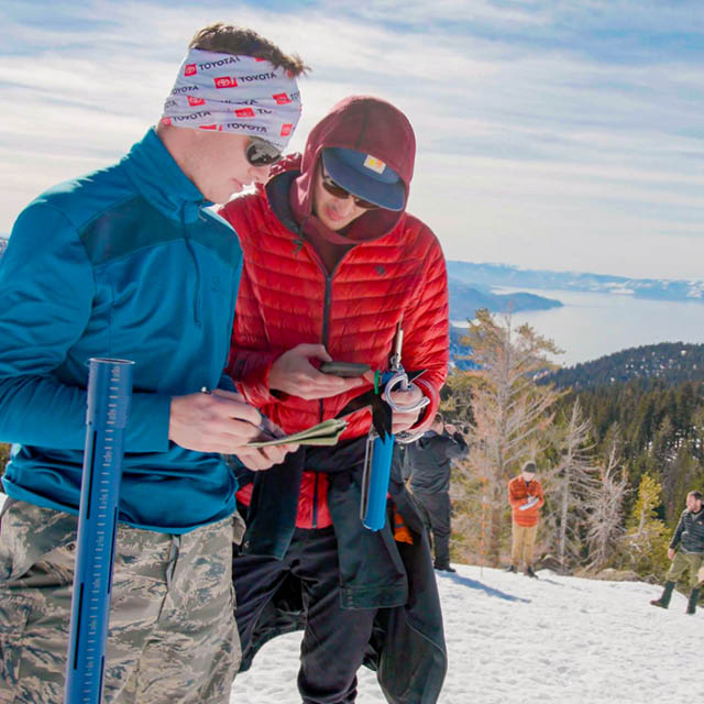 Two students look at snow under a magnifying glass outside at Lake Tahoe.