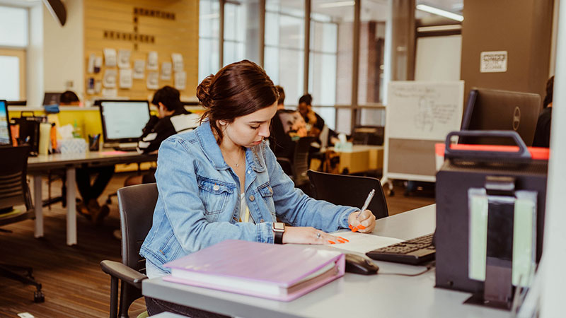 A student sits at a desk reading writing in a notebook