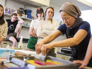 A professor in an art studio working with paint with five students watching the process  