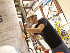 A person in an earthquake engineering lab inspecting a large concrete pillar for damage from a test