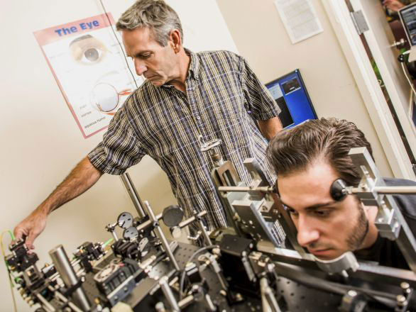 Researcher standing with a test subject with their head held in position on a test stand working on an experiment relating to the neuroscience of vision