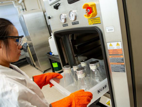A researcher loading a tray of labware bottles into an autoclave in the Applied Research Facility.