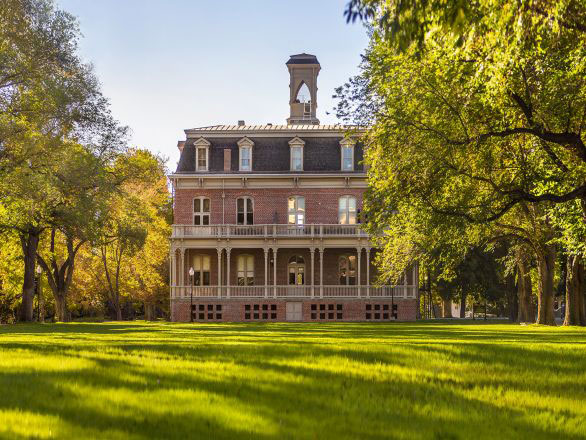 View of Morrill Hall at the University of Nevada, Reno in the summer surrounded by green grass and trees.