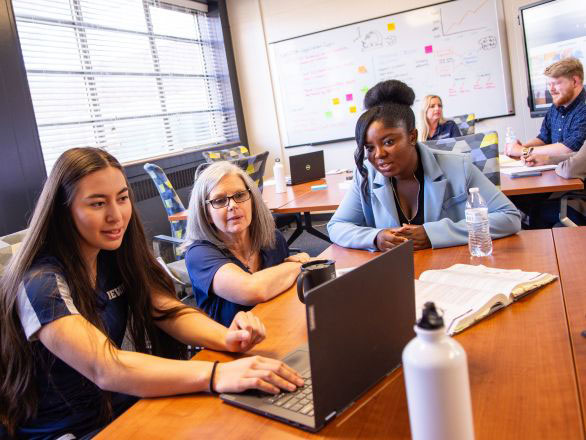 Two studens and a faculty member working together at a table with a laptop in the Applied Research Facility..