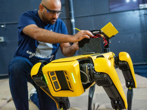 A student researcher working with a robot walking on four legs.