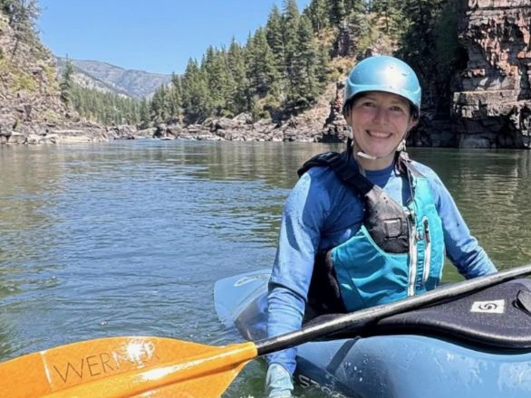 A woman in a blue helmet and vest paddling a blue kayak.