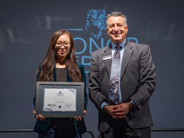 Ying Yang and Brian Sandoval smile for a photo, with Yang holding a framed certificate.