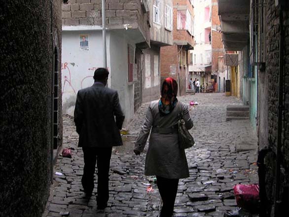 Two people walk in an alleyway over cobblestone streets.