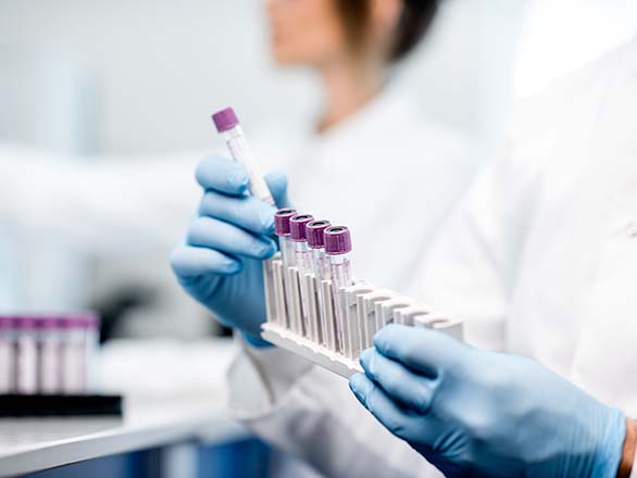 A gloved lab technician holding test tubes with purple caps in a lab.