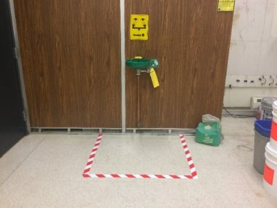 An eyewash station with safety tape marking an area on the floor around it