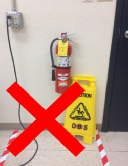 A fire extinguisher which has been unsafely blocked by a sign and a tripping hazard