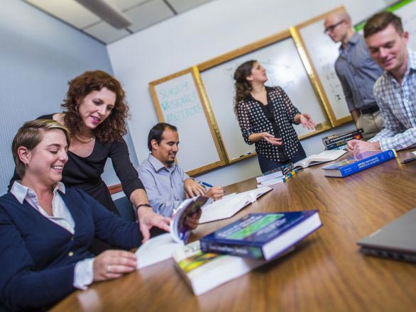 Students and faculty researchers gathered in a conference room around a table with books and a whiteboard