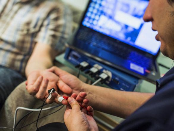 Graduate student researcher putting a sensor on a research participants finger with a laptop in the background