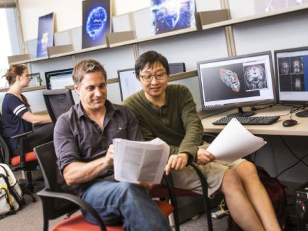 Neuroscience student and mentor in a computer lab with brain imaging photos around the room