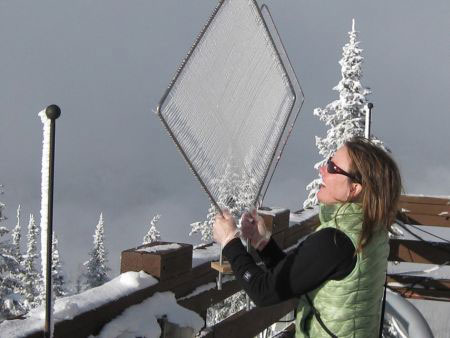 Student in earth sciences at a snowy research station, standing outside holding up sampling equipment (looks like a screen)