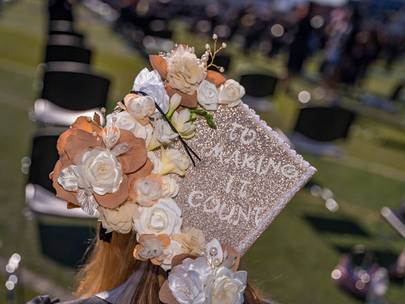 A graduation cap, seen from the back, decorated with brown and white flowers and reading "To Making it Count."