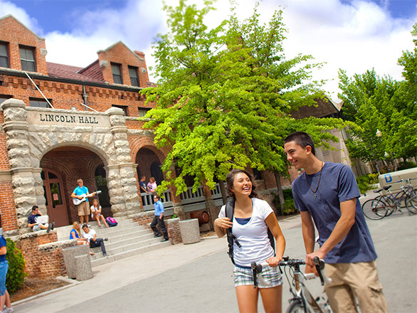 A student walks their bike while talking to another student in front of Licoln Hall, while other students chat near the building on the campus of the University of Nevada, Reno.
