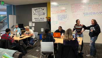 Students in the Veteran and Military Center, studying, talking and working. A wall-sized whiteboard displays reminders and tips.