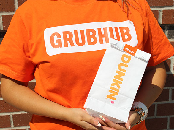 Person wearing orange Grubhub tshirt and holding a bag of Dunkin' Donuts