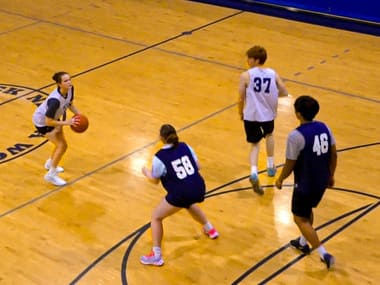 Students participate in an intramural basketball game at the E. L. Wiegand Fitness Center. One player prepares to shoot while teammates and defenders position themselves on the indoor court during active gameplay.