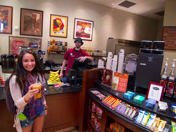 A student and an employee in a coffee shop; the student is holding a drink and the employee is standing behind the counter.