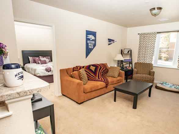 A room in Ponderosa Village, with a couch, chair, table, pet bed and door opening to a bedroom in the background