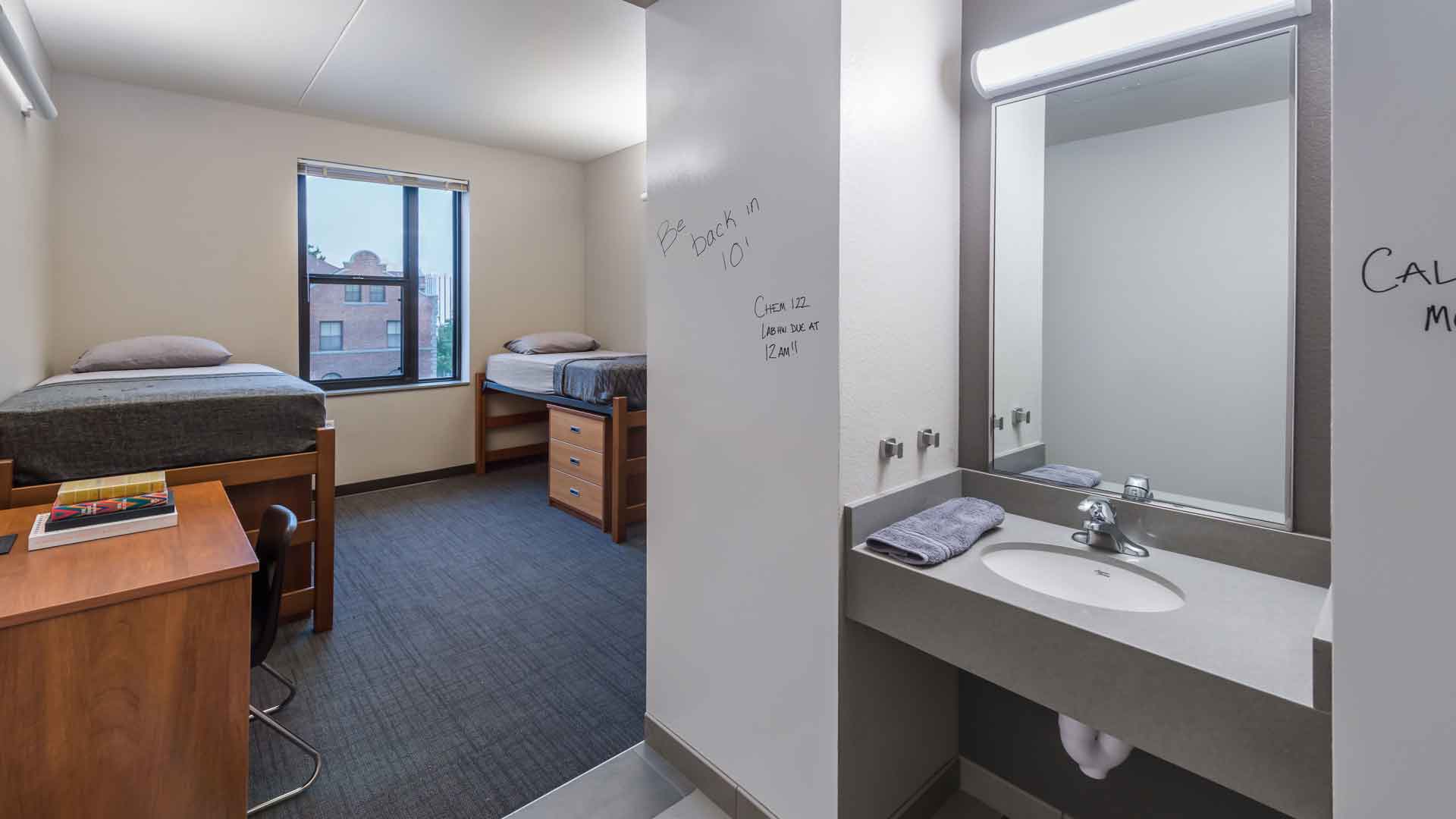 An empty dorm room in Great Basin Hall, with two beds, lifted off the floor, and a sink and mirror. 