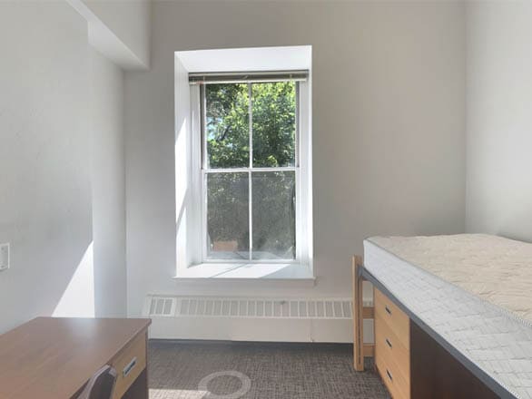 Bright single dorm room in Manzanita Hall with a large window, a raised bed with drawers underneath, and a wooden desk with chair.