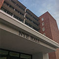 View of Nye Hall, a multi-story brick and concrete building with balconies and large windows, seen from the entrance canopy.