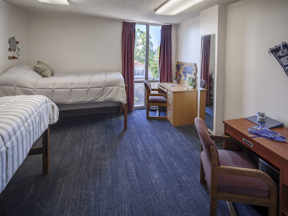 Spacious double bedroom at Sierra Hall with two twin beds, individual desks and chairs, a large window with curtains, and a full-length mirror.