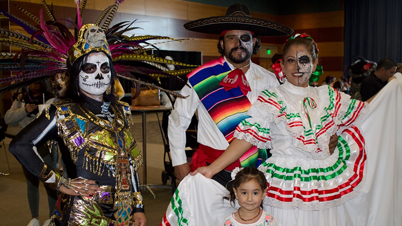 Three people celebrating during Latinx Heritage celebration in Día de Muertos costumes and traditional dress.