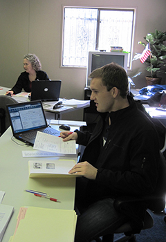 Colby Cross, an accounting student works at a table with a computer and papers