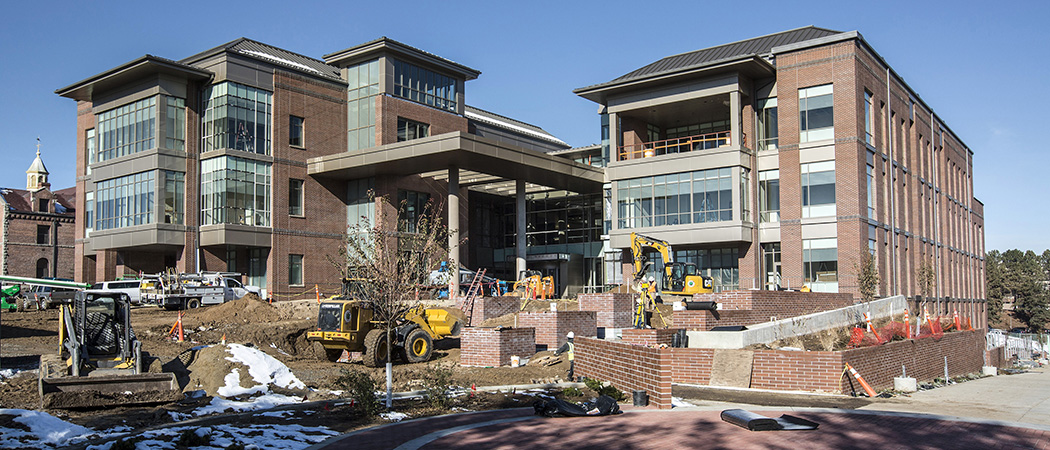 A view of the Pennington Student Achievement Center at the University of Nevada, Reno, a multi-story brick building with large bay windows, trees in front and a courtyard with a statue of Senator Richard Bryan.